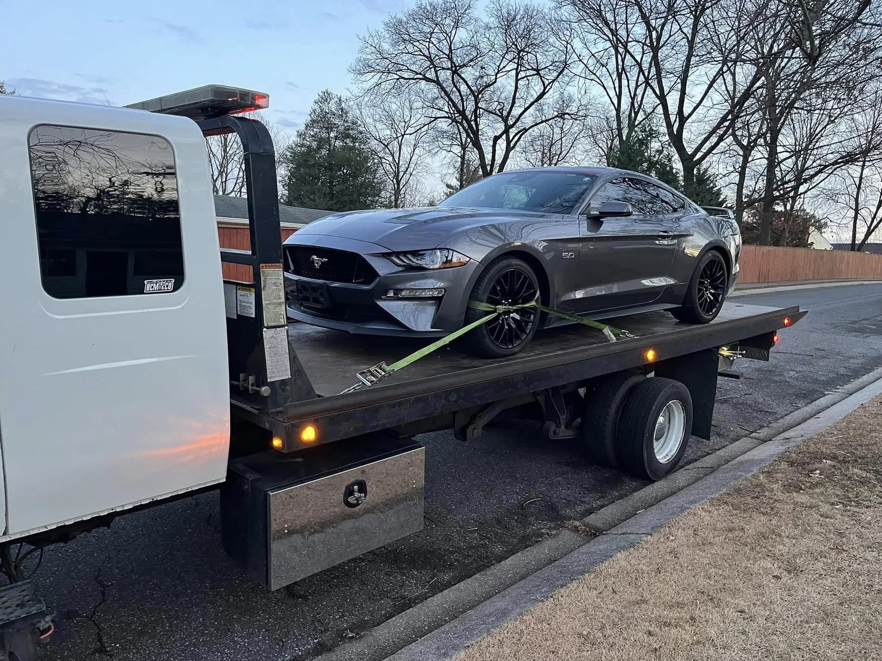 Flatbed tow truck transporting a gray Ford Mustang